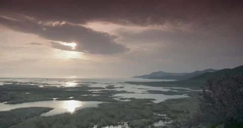 Tranquil lake surrounded by traffic and bushes under a cloudy sky during sunset Stock Footage 246987526
