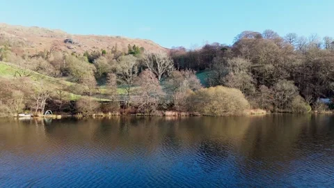 Tranquil lakeside scene with trees and a mountain under a clear blue sky. Stock Footage 293790304