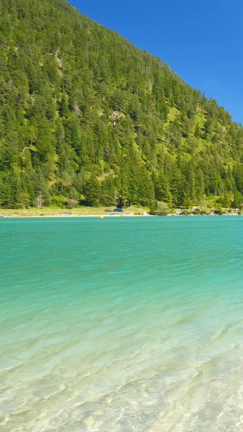 Tranquil lakeside view of an emerald alpine lake framed by forested peaks and Stock Footage 308299850