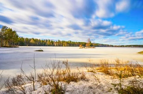 A tranquil landscape of sun lit cloudscape over a frozen lake surrounded by p Stock Photos