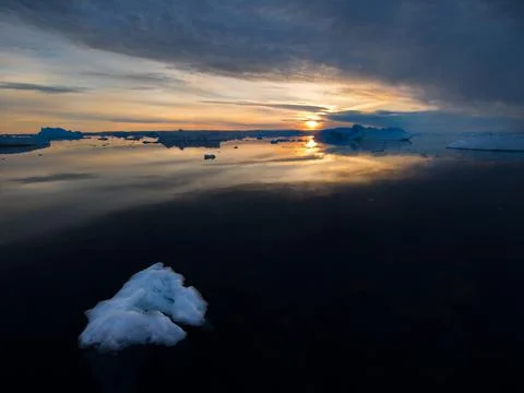 A tranquil low angle view of arctic waters at sunset with a small iceberg  Stock Photos
