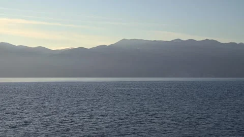 Tranquil ocean horizon with distant mountain silhouette at sunset Stock Footage 331261301
