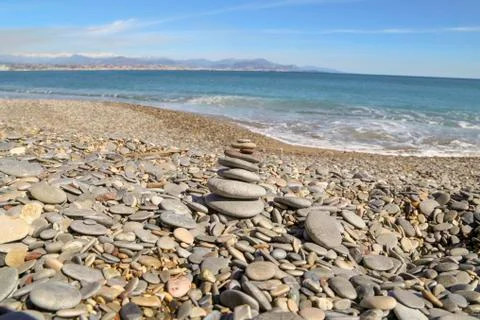 Tranquil ocean with no waves a small sandy beach with pebbles all around Stock Photos