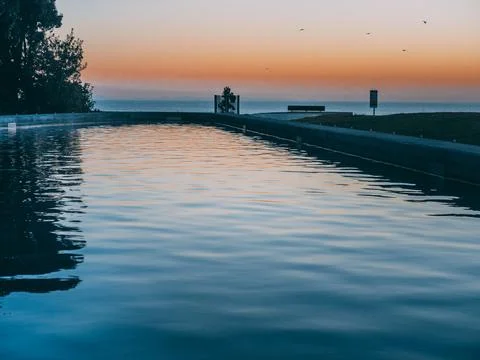 Tranquil ocean pool reflecting warm sunset sky at dawn Stock-Fotos