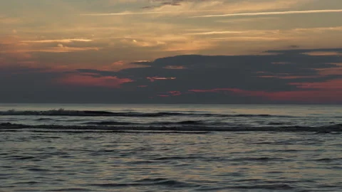 Tranquil ocean waves under glowing sunset sky with layered clouds and calm Stock Footage 345125173