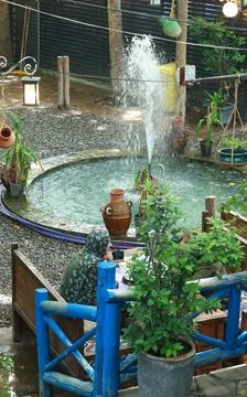 A tranquil outdoor cafe setting featuring a circular water fountain, lush green Stock Photos