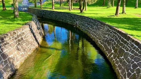 A tranquil park with a stone wall, river, pond, and charming bridge Stock Photos
