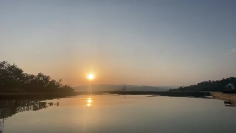 Tranquil pool reflecting vibrant sunset with hill and clear sky 🌄💦 動画素材 310965194