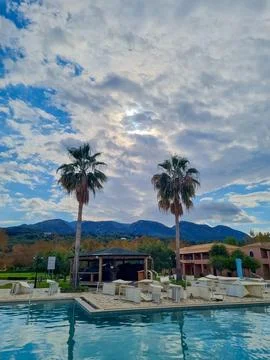 A tranquil poolside scene with palm trees, a bar area, lounge chairs, and m.. Stock Photos