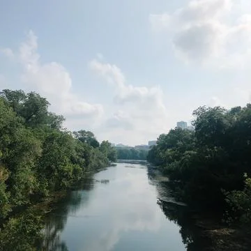 Tranquil river with lush trees and a distant city skyline Stock Photos