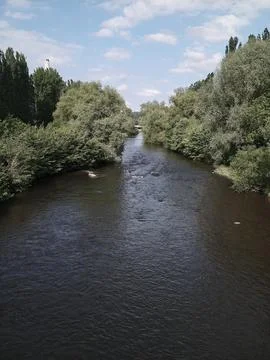Tranquil River Moves Smoothly Under Expansive Bright Sky With Clouds Stock Photos