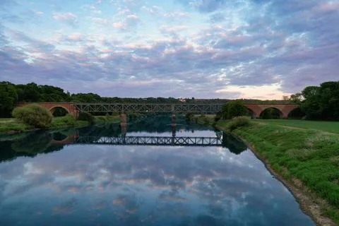 Tranquil river reflection under a bridge at dusk Stock Photos