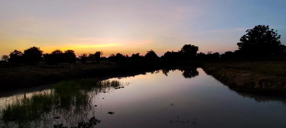 A tranquil river view with the sun setting over the calm waters and clear sky. Stock Photos