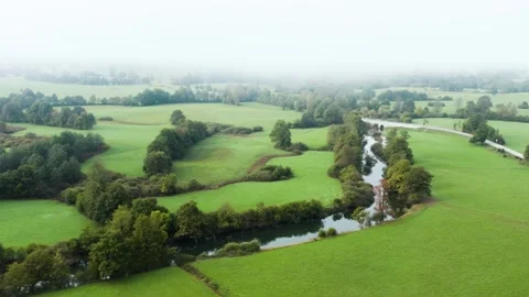 A tranquil river winds through a lush, fog-covered landscape, with green fields. Stock Footage 287115006