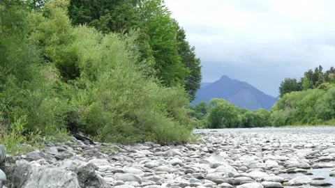 Tranquil Riverbank Surrounded by Lush Greenery and Majestic Mountains in Nature Stock Footage 303479804