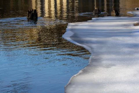 Tranquil riverside view with ice remnants along the shore during a sunny wi.. Stock Photos