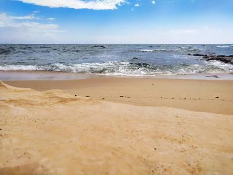 A tranquil sandy beach with gentle waves crashing under a bright blue sky. Th Stock Photos