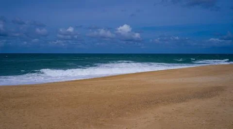 Tranquil scene of waves crashing on a sandy beach under a cloud-dotted sky Fotos de archivo