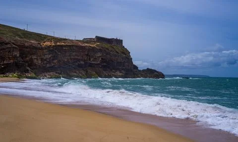 Tranquil scene of waves crashing on a sandy beach under a cloud-dotted sky 스톡 사진