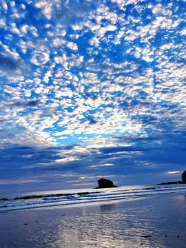 Tranquil sea stack rock formation in ocean under dramatic altocumulus cloudscape Stock Photos
