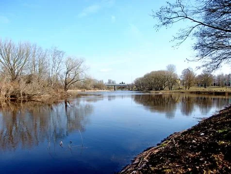 Tranquil Spring River: Calm Water Reflecting Clear Sky, and Bridge in Distance Stock Photos