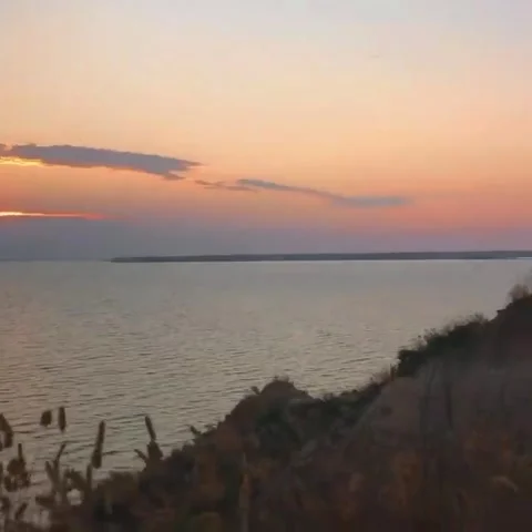 Tranquil Sunset Over Water with Orange Sky and Rocky Shoreline in Foreground Stock Footage 309959898