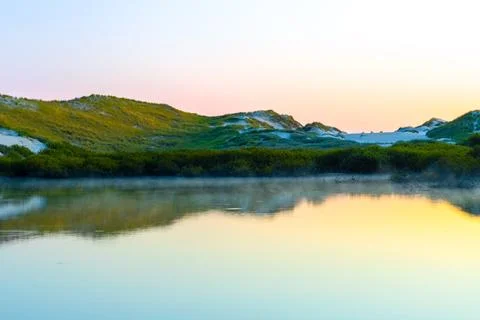 Tranquil sunset reflection over calm water surrounded by lush greenery and Stock Photos