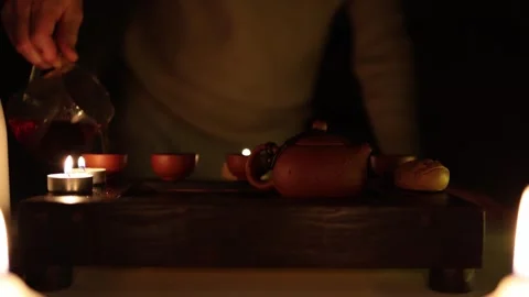 A tranquil tea ceremony setting lit by candlelight, featuring a glass pitcher po Video stock 299384265