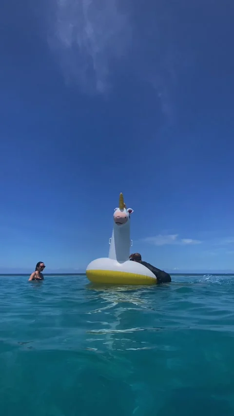 Tranquil turquoise ocean with floating unicorn and family leisure time Stockbeeldmateriaal 335712992
