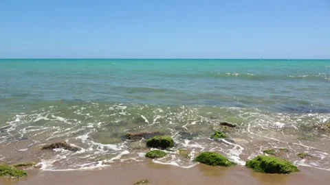 Tranquil turquoise sea gently lapping on a rocky beach on a sunny day Stock Footage 283535199