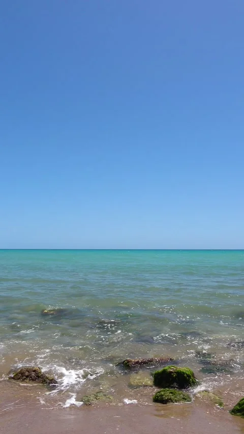 Tranquil turquoise sea gently lapping on a rocky beach on a sunny day Stock Footage 283539113