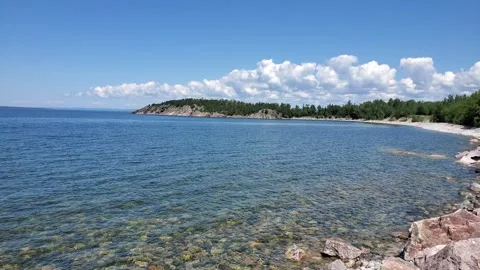 A tranquil view of a clear lake surrounded by greenery and rocky shores Stock-Footage 316301466
