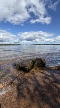 Tranquil view of a wet boulder in shallow transparent lake water with a distant Stock Photos