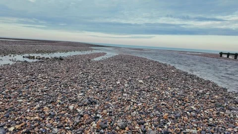 Tranquil walk on pebble beach with sea groynes and distant cliff view Stock Footage 309767203