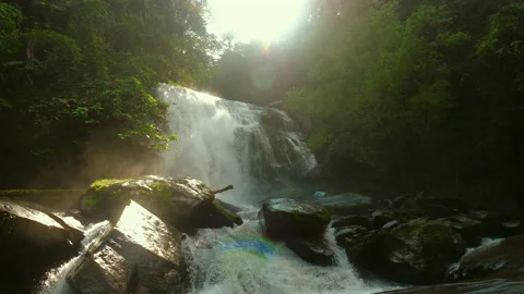 Tranquil waterfall cascading over rocks in lush forest, bathed in Stock Footage 281276411