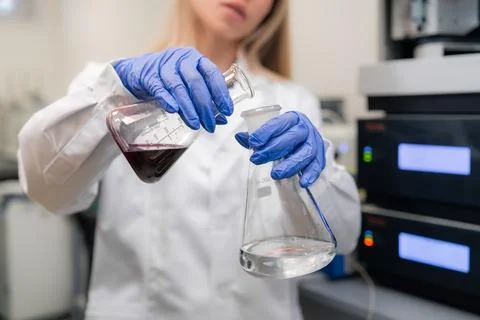 Transferring dark red liquid from volumetric flask to other at pharmaceutical Stock-Fotos