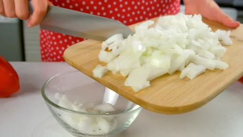 Transferring diced chopped onions from cutting board to glass bowl on kitchen. Stock Footage 312399173