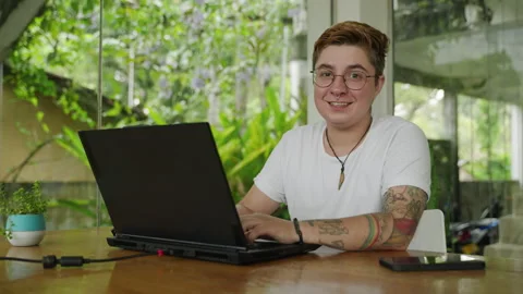 Transgender pro smiles while using laptop in modern office. Happy individual Stock Footage 270535546