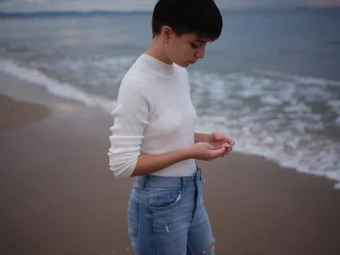 Transgender on the seashore looking at a shell she is holding in her hand Stock Photos