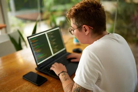 Transgender web developer works on laptop, programming in modern eco office Fotos de archivo