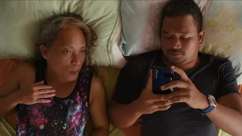 Transgender woman talking while man is using phone in bed Stockbeeldmateriaal 334370620