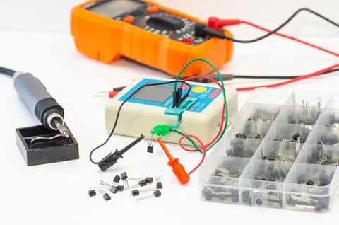 Transistor tester and instruments, a soldering iron, and tools lie on a white ba Stock Photos