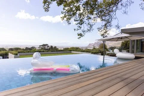 Translucent lounger is floating in infinity pool by wooden deck, with pink Foto stock