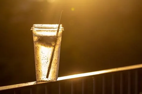 A translucent plastic cup with straw with condensation in the warm light Stock Photos