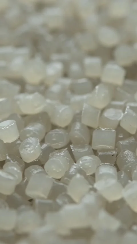 Translucent plastic pellets rotate in macro view, creating abstract industrial Stock Footage 334657482