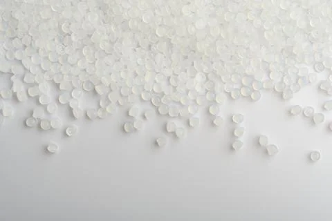 Translucent polymer pellets scatter across white surface, industrial backgrou Stock Photos