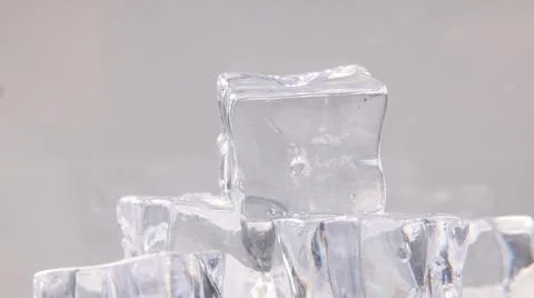 A translucent square ice cube balanced on top of a pile of melting ice cubes Stock Photos