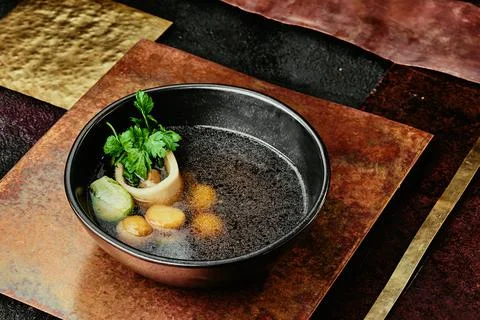 Transparent beef broth with bone, garnished with parsley and Brussels sprouts in Stock Photos