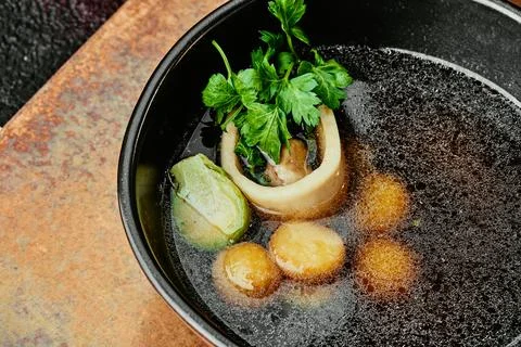 Transparent beef broth with bone, garnished with parsley and Brussels sprouts in Stock Photos