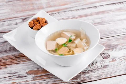 Transparent beef broth with egg, garnished with dill in a white bowl on a wooden Stock Photos